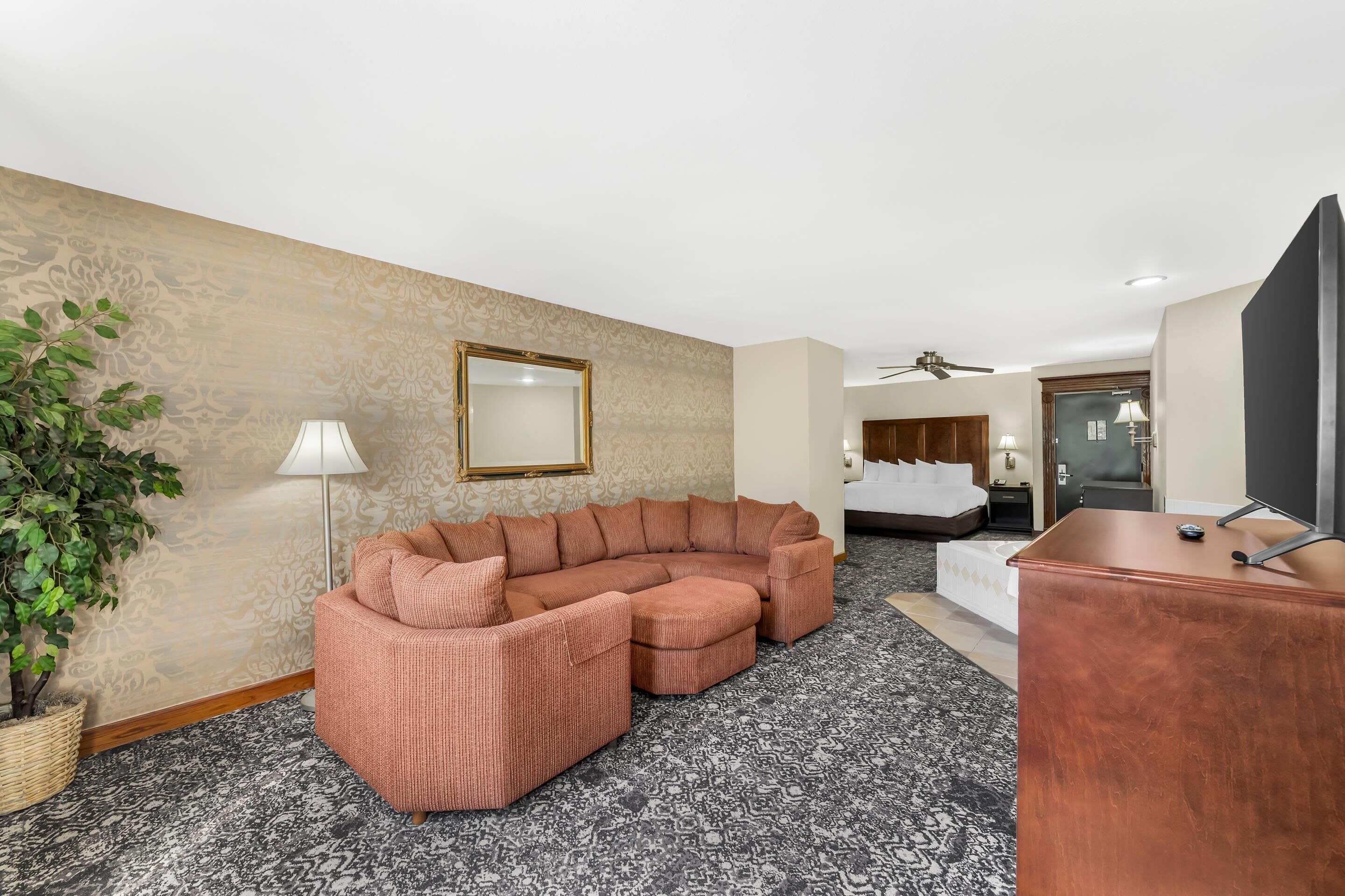 Habitación de hotel con sofá modular, escritorio, televisión, ventilador de techo, cama y planta en maceta.