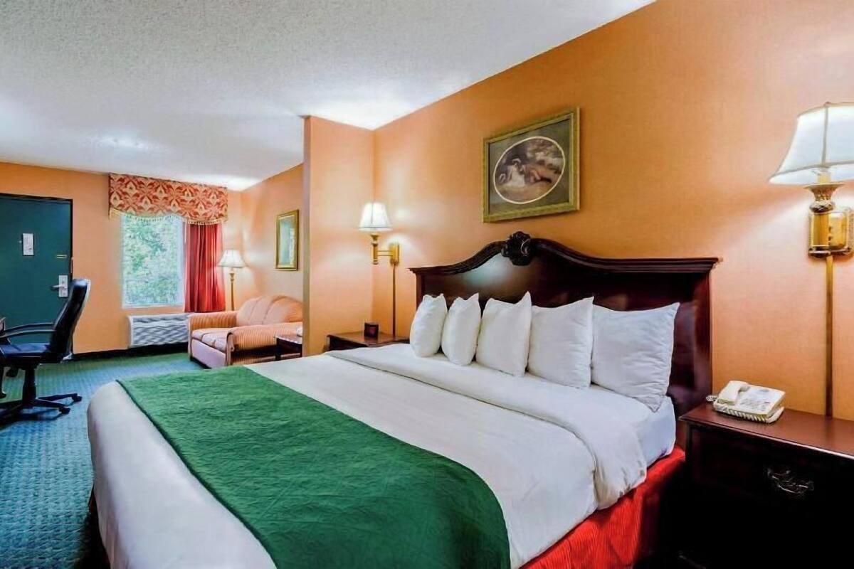 A hotel room with a bed, a desk, a chair, a lamp, and a painting on the wall.