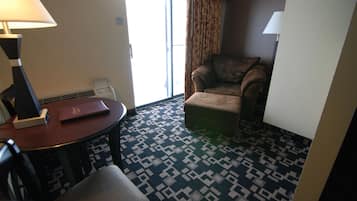 Et hotelværelse med et mønstret tæppe, en sofa, et lille bord med en lampe og udsigt gennem en dør.