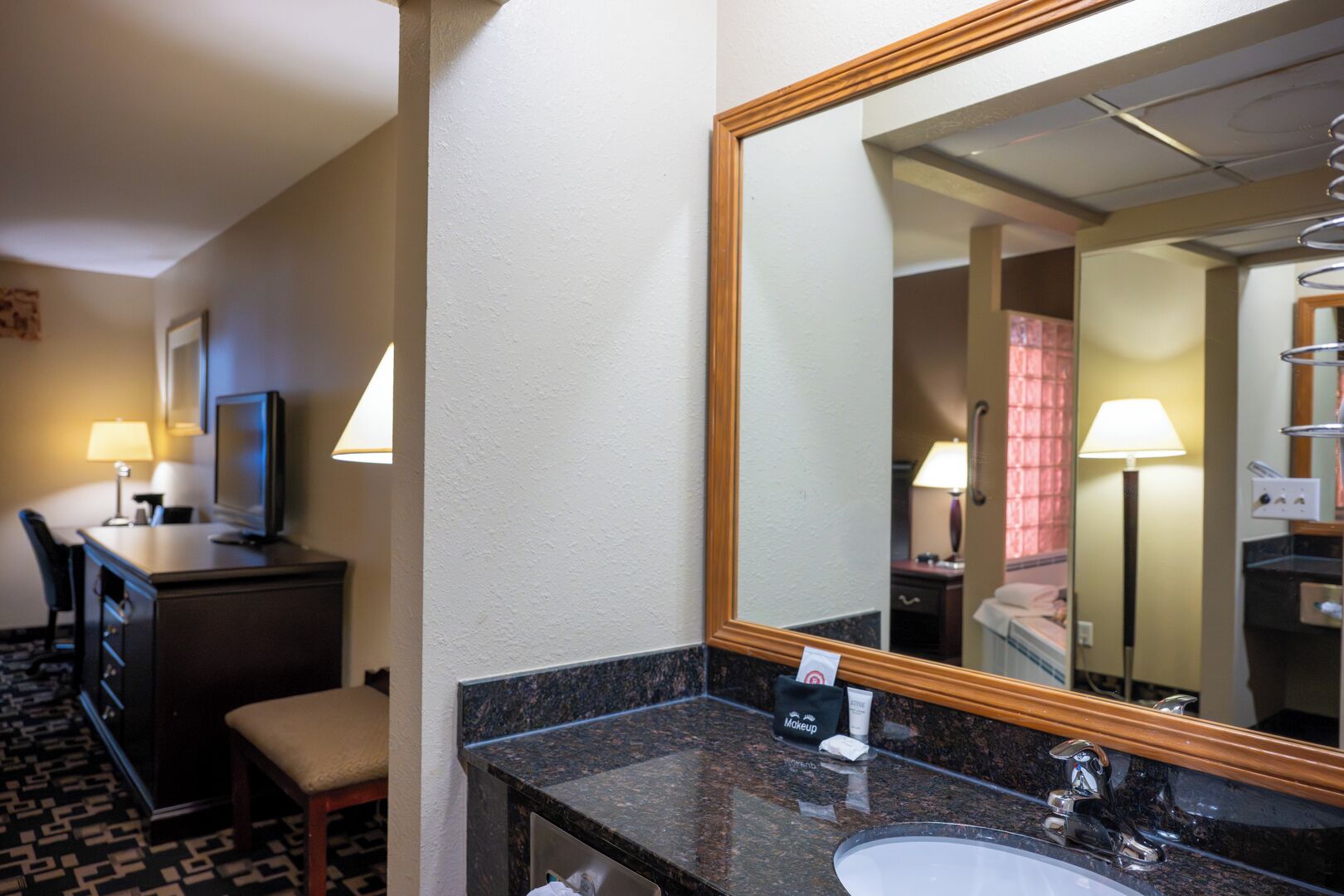 Habitación de hotel con escritorio, silla, televisor y un espejo grande.