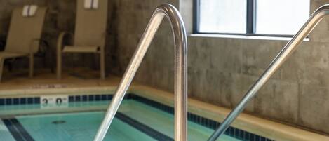 A swimming pool with metal handrails, tiled walls, and a window in the background.