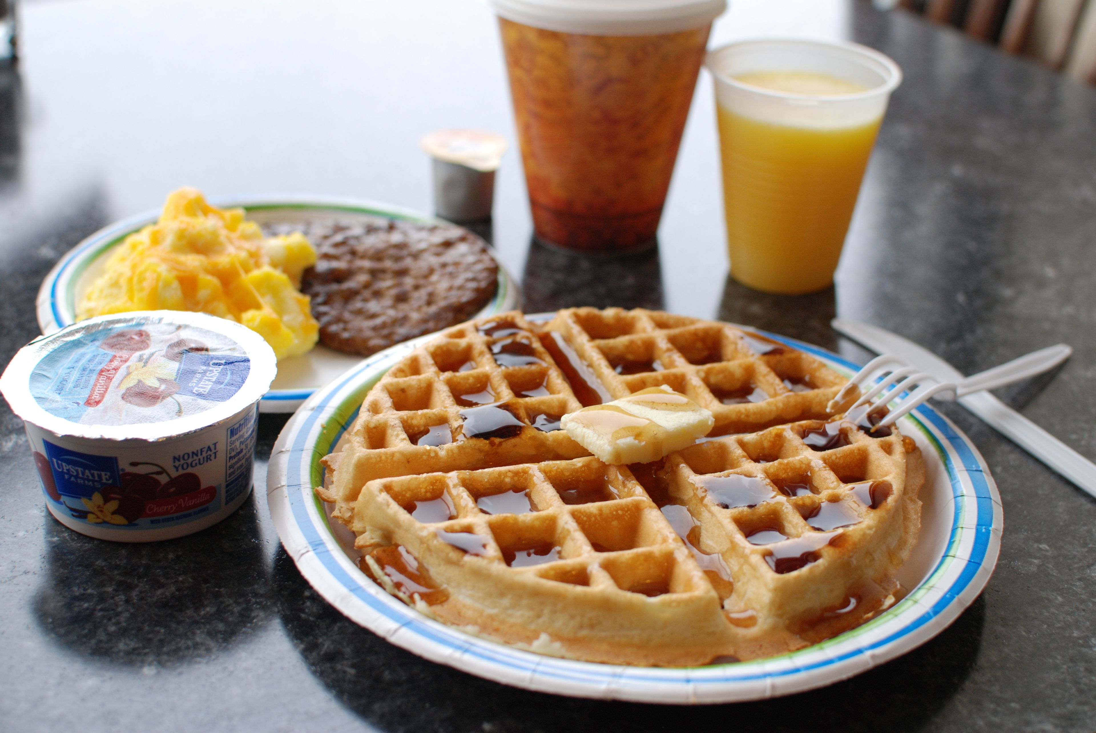 A breakfast plate with waffles, syrup, and a cup of orange juice.