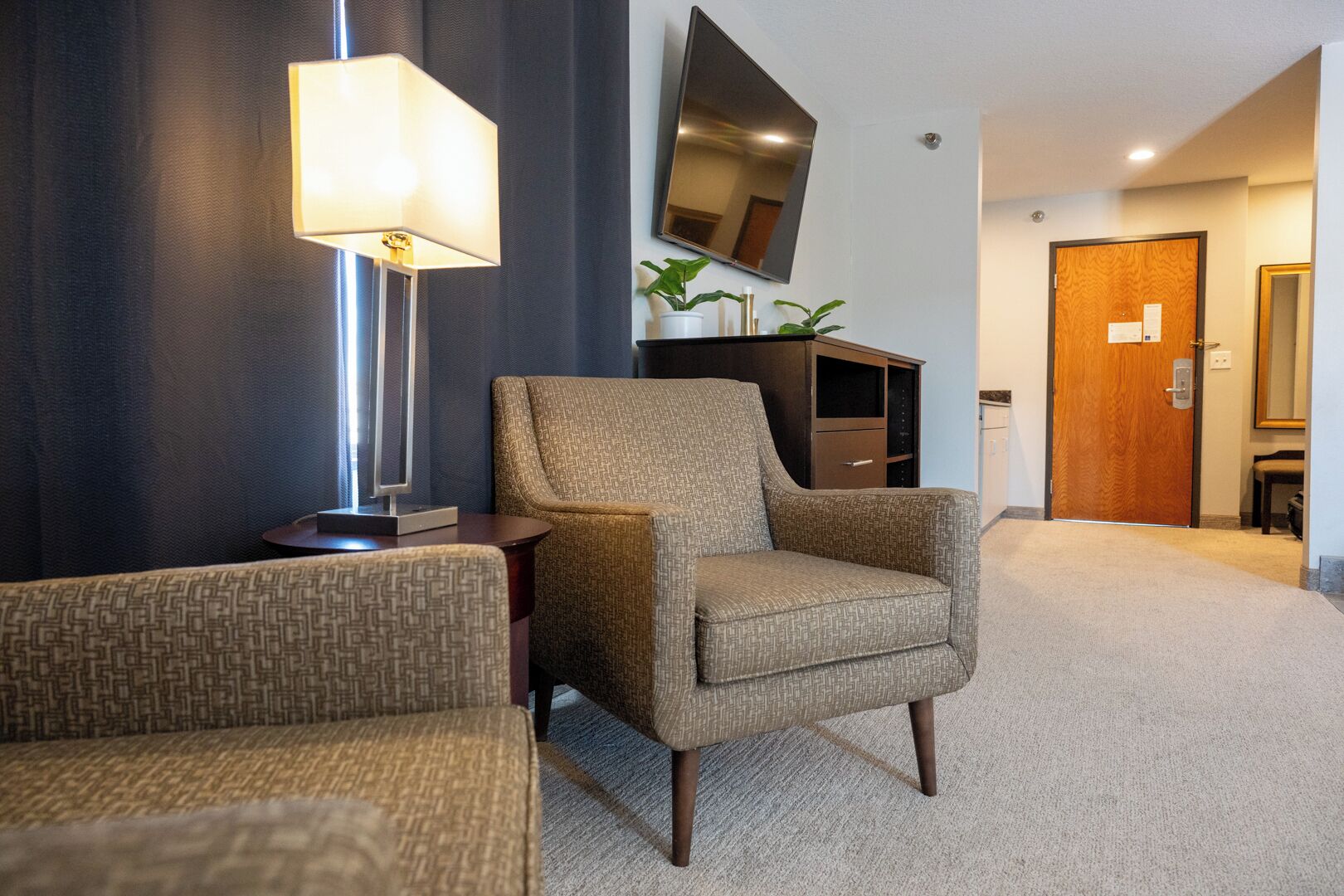 A modern living room with a sofa, armchair, and a flat-screen TV mounted on the wall.