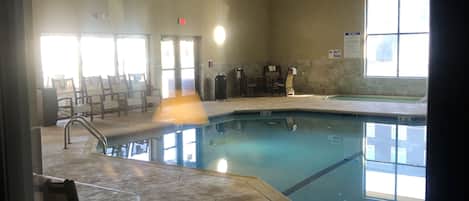 An indoor swimming pool with a caution sign, a seating area, and a view of the pool area.