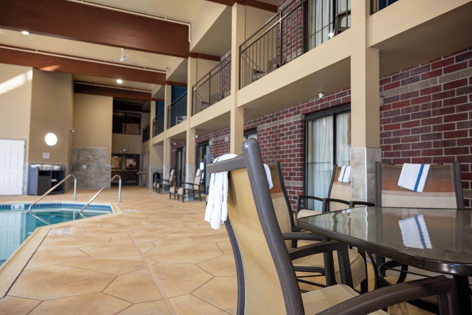 A pool area with a glass table and chairs, a brick wall, and a balcony with railings.