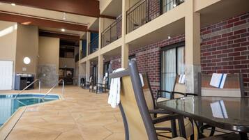 A pool area with a glass table and chairs, a brick wall, and a balcony with railings.