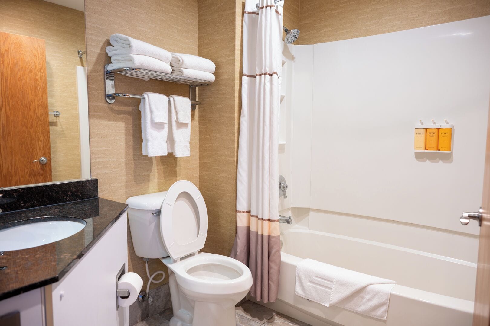 A bathroom with a toilet, sink, and bathtub. There are towels on a rack and a shower curtain.