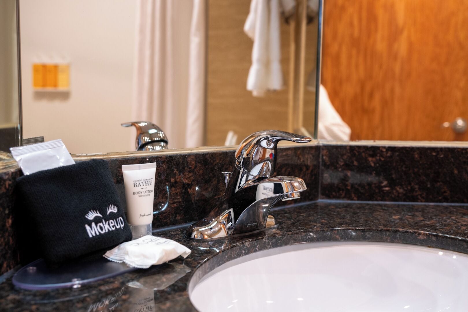 Un baño con lavamanos, espejo, toallero y artículos de aseo, incluyendo un neceser y una crema corporal.