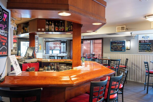 A bar area with a wooden counter, red cushioned chairs, and a menu board on the wall.