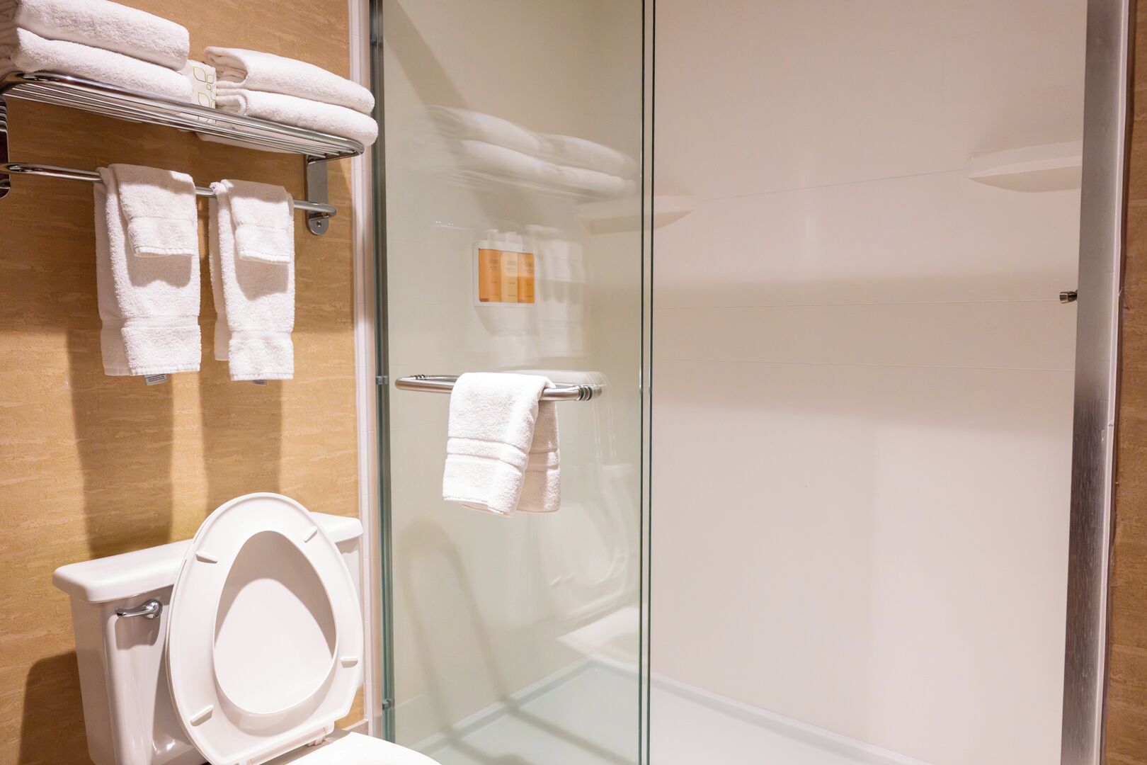 Ein modernes Badezimmer mit Duschkabine aus Glas, Toilette und Handtuchhalter mit gefalteten Handtüchern.