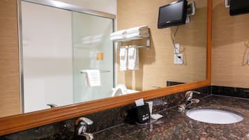 Un bagno d'hotel con cabina doccia in vetro, due lavabi con specchiette a muro, una televisione montata e un portaservizi con asciugamani piegati.