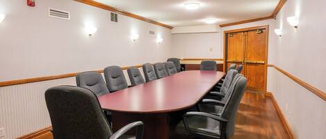 Un salón de conferencias con una larga mesa, varias sillas, una puerta de madera y luces fijadas a la pared.