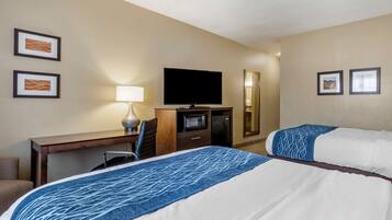 A hotel room with two beds, a desk, a television, a lamp, and framed artwork on the walls.