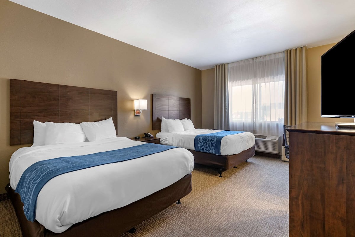 Une chambre d’hôtel avec deux lits, un bureau, une télévision et une fenêtre avec des rideaux.