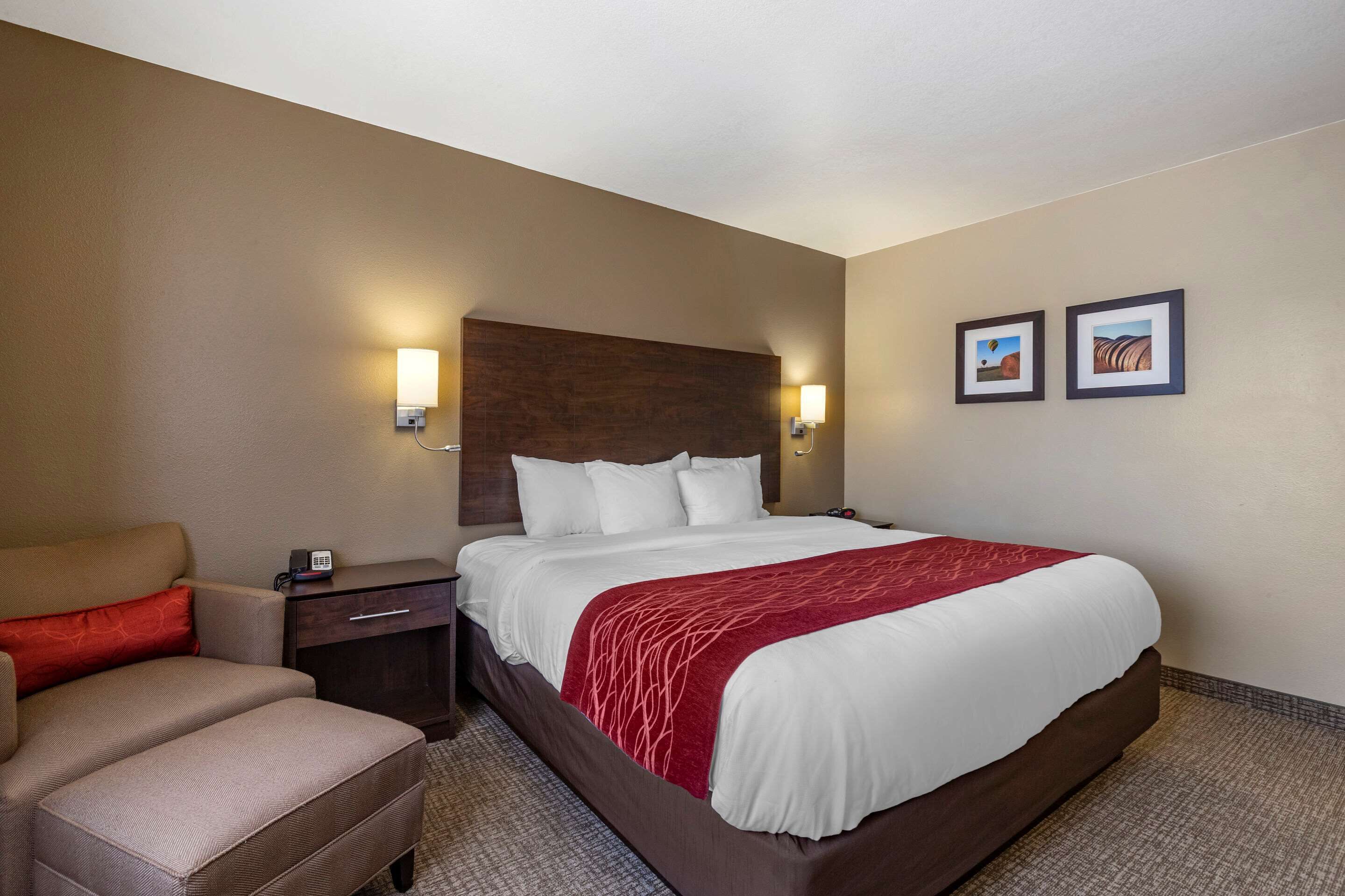 A hotel room with a large bed, a bedside table, a chair, and two wall-mounted lights.