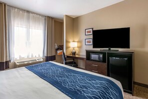 A hotel room with a bed, a desk with a computer, a television, and a refrigerator.