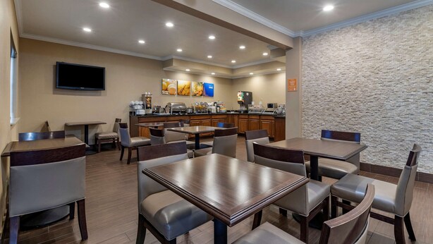 A hotel dining area with multiple tables and chairs, a kitchen in the background, and a stone wall. - Comfort Inn & Suites Waterloo - Cedar Falls (Waterloo)