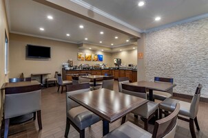 Un comedor de hotel con varias mesas y sillas, una cocina al fondo y una pared de piedra.