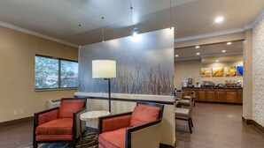 A hotel lobby with two armchairs, a small round table, a bar area, and a kitchen in the background. - Comfort Inn & Suites Waterloo - Cedar Falls (Waterloo)
