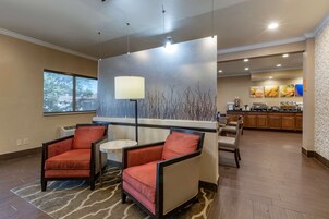 A hotel lobby with two armchairs, a small round table, a bar area, and a kitchen in the background.