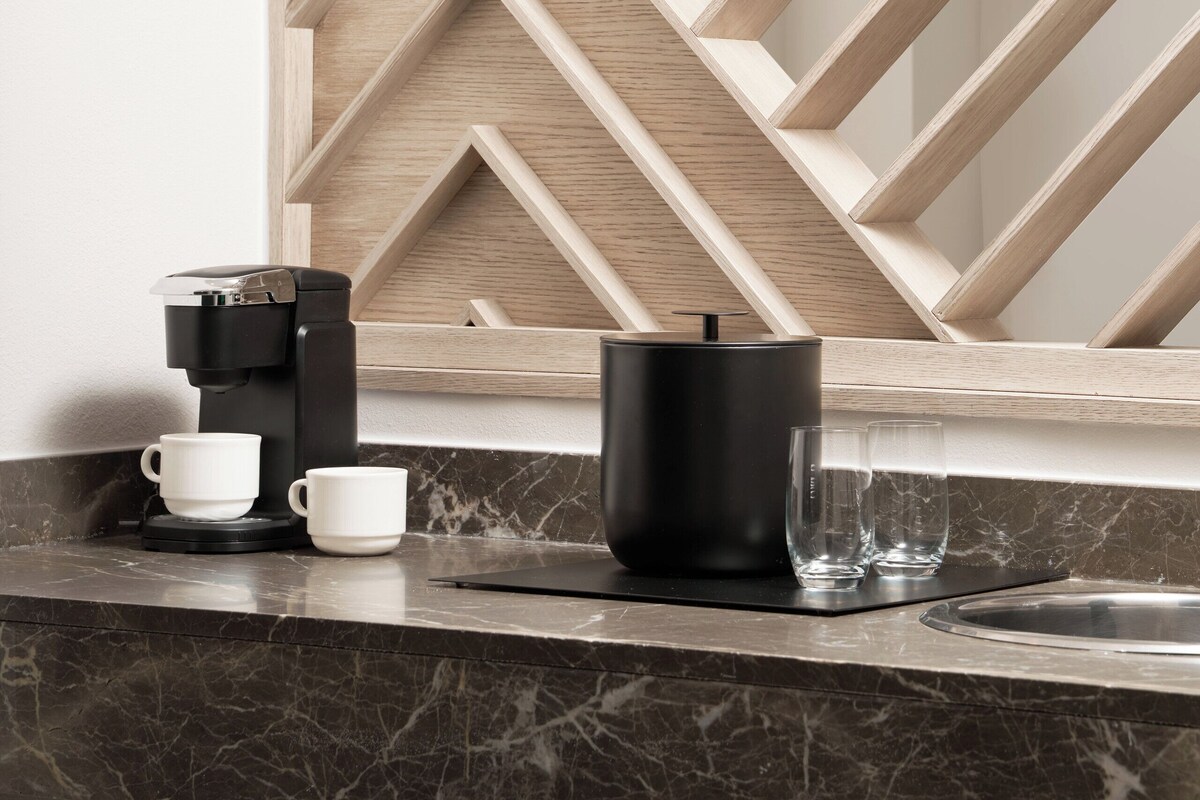 Una cocina moderna con encimera de mármol, una cafetera, una taza negra y un vaso.