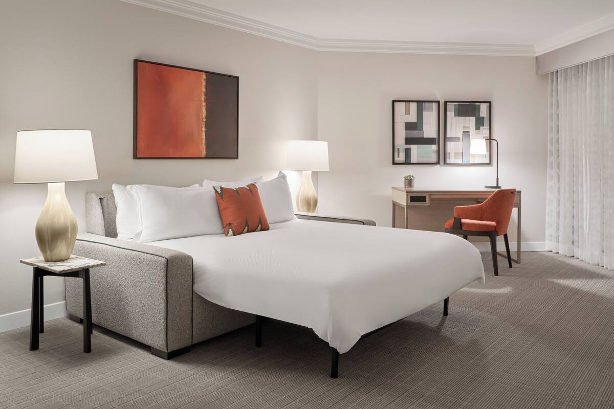 A hotel room with a large bed, two bedside tables with lamps, a desk, and a chair.