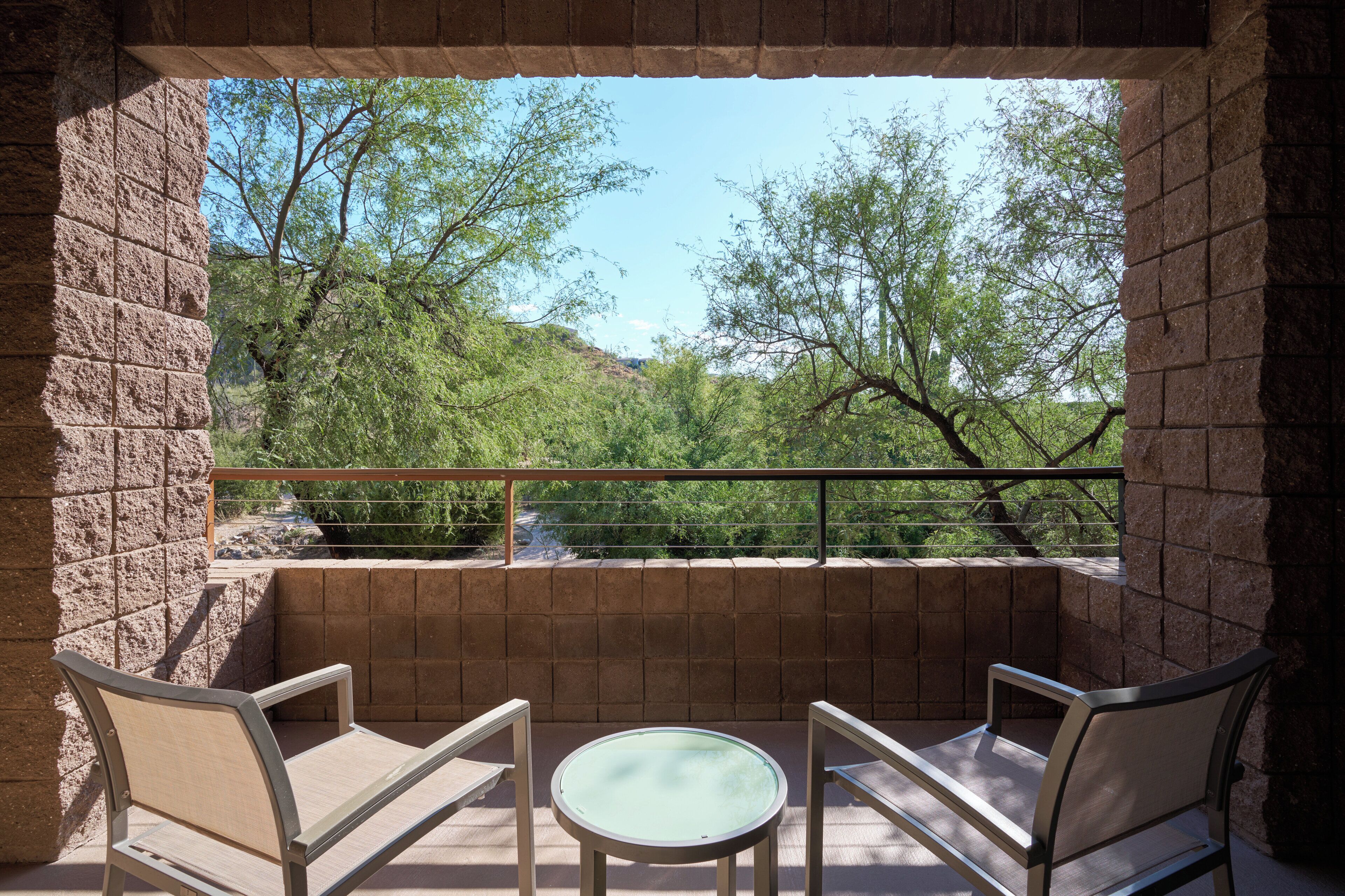 Un balcon avec deux chaises et une table, donnant sur un paysage arboré et un ciel dégagé.