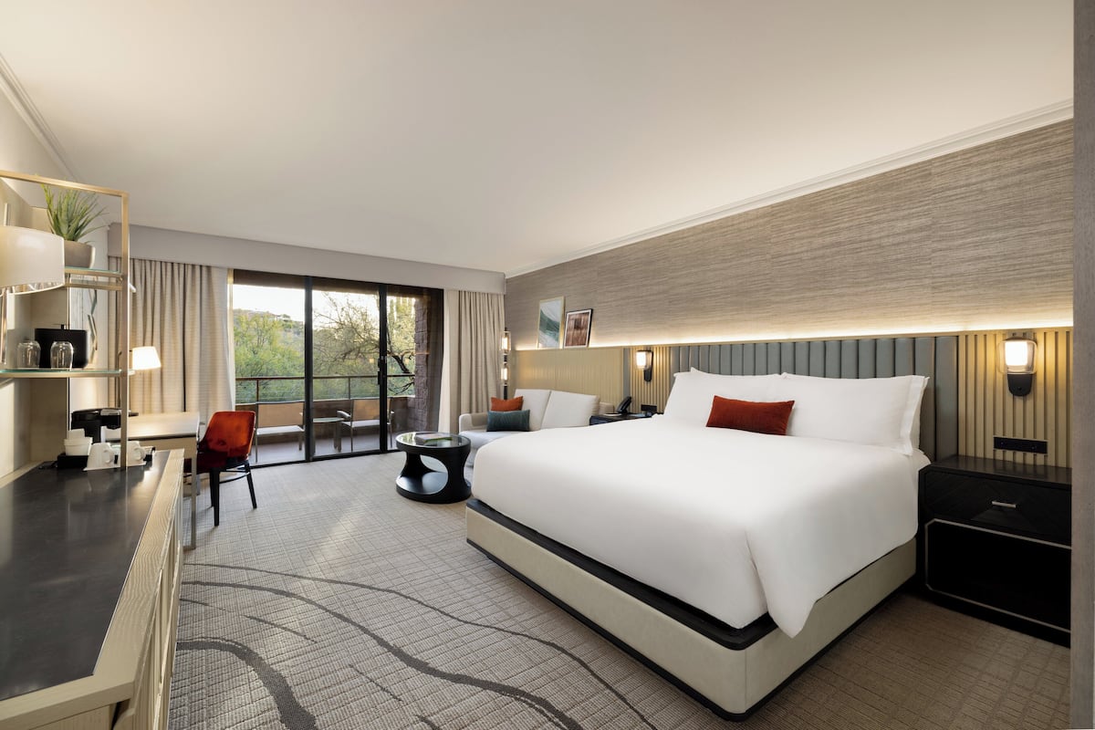 A modern hotel room with a large bed, a desk, a chair, and a view of the outdoors.