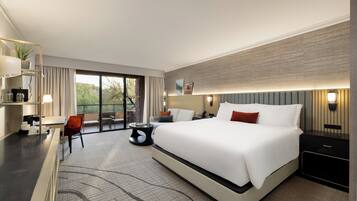 A modern hotel room with a large bed, a desk, a chair, and a view of the outdoors.