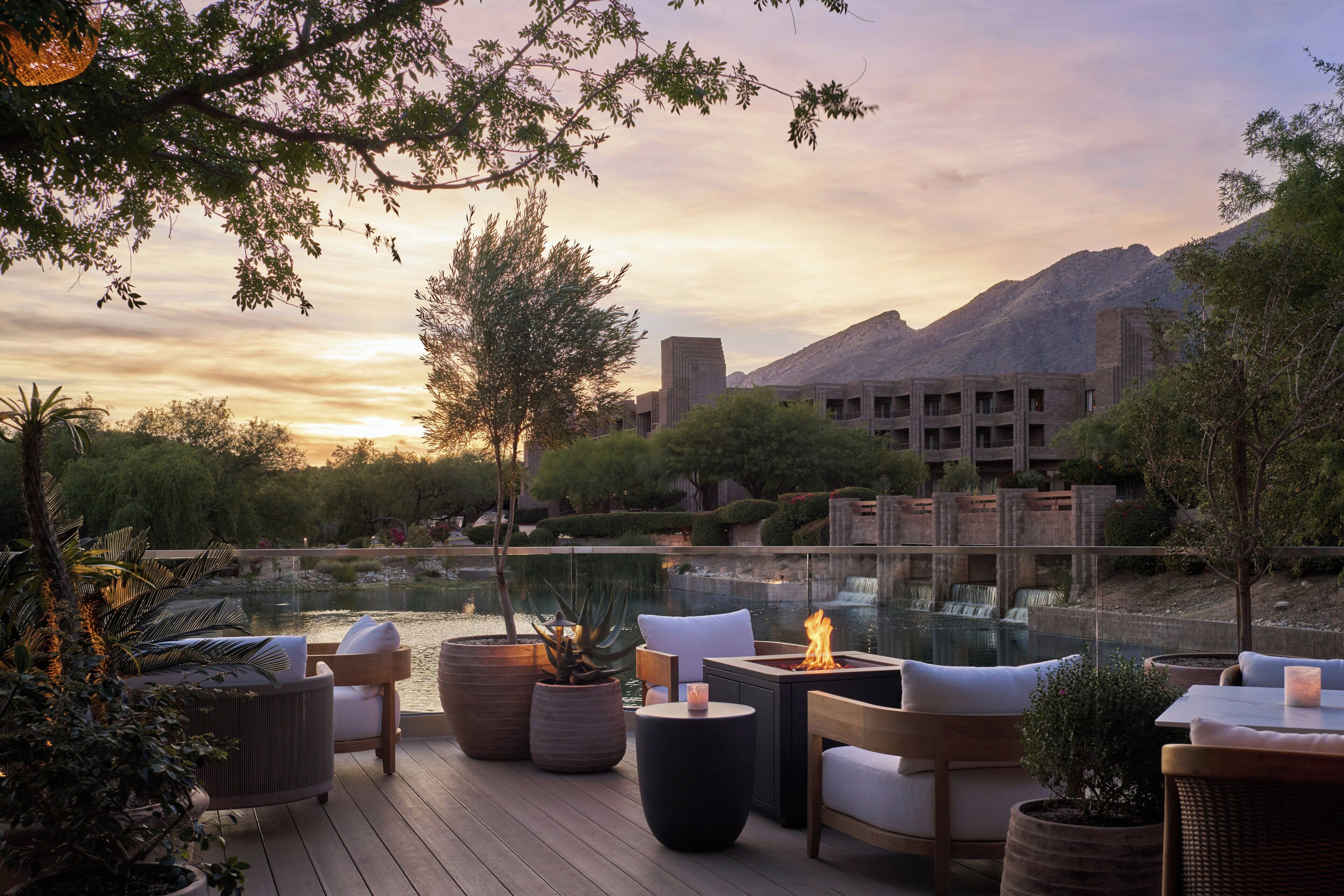 A deck with outdoor seating, a fire feature, and a view of a mountain and building in the background.