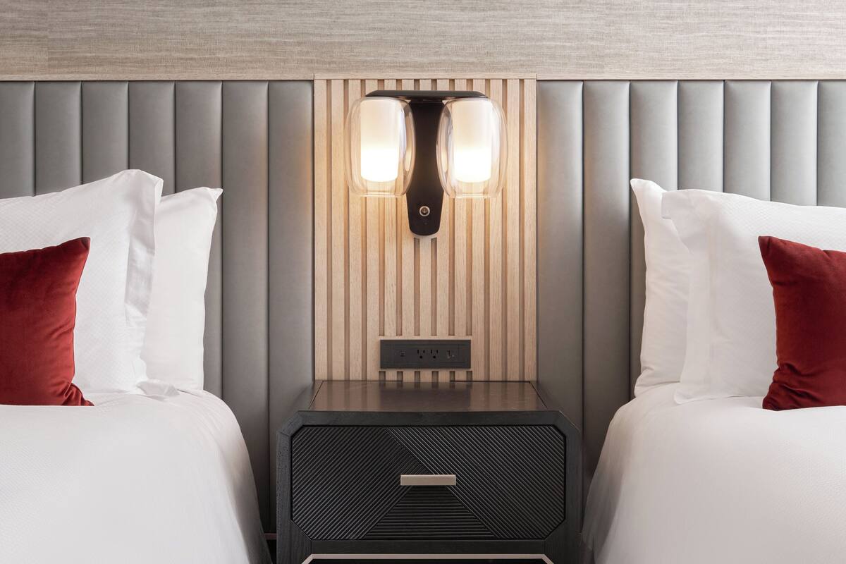 A hotel room with two beds, a nightstand with a lamp, and a wooden panel wall.