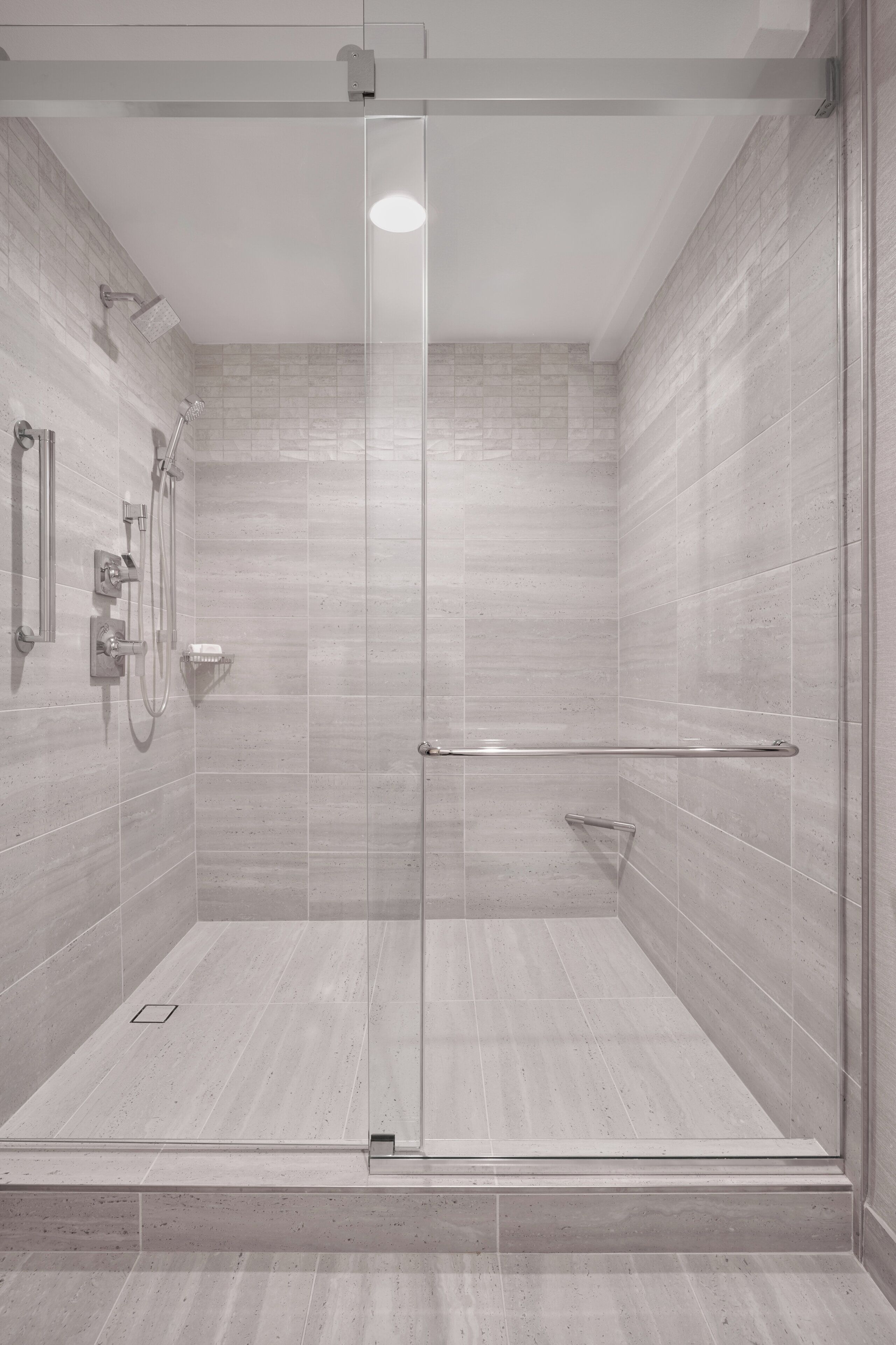 A modern shower with a glass door, a handheld showerhead, and a wall-mounted faucet.