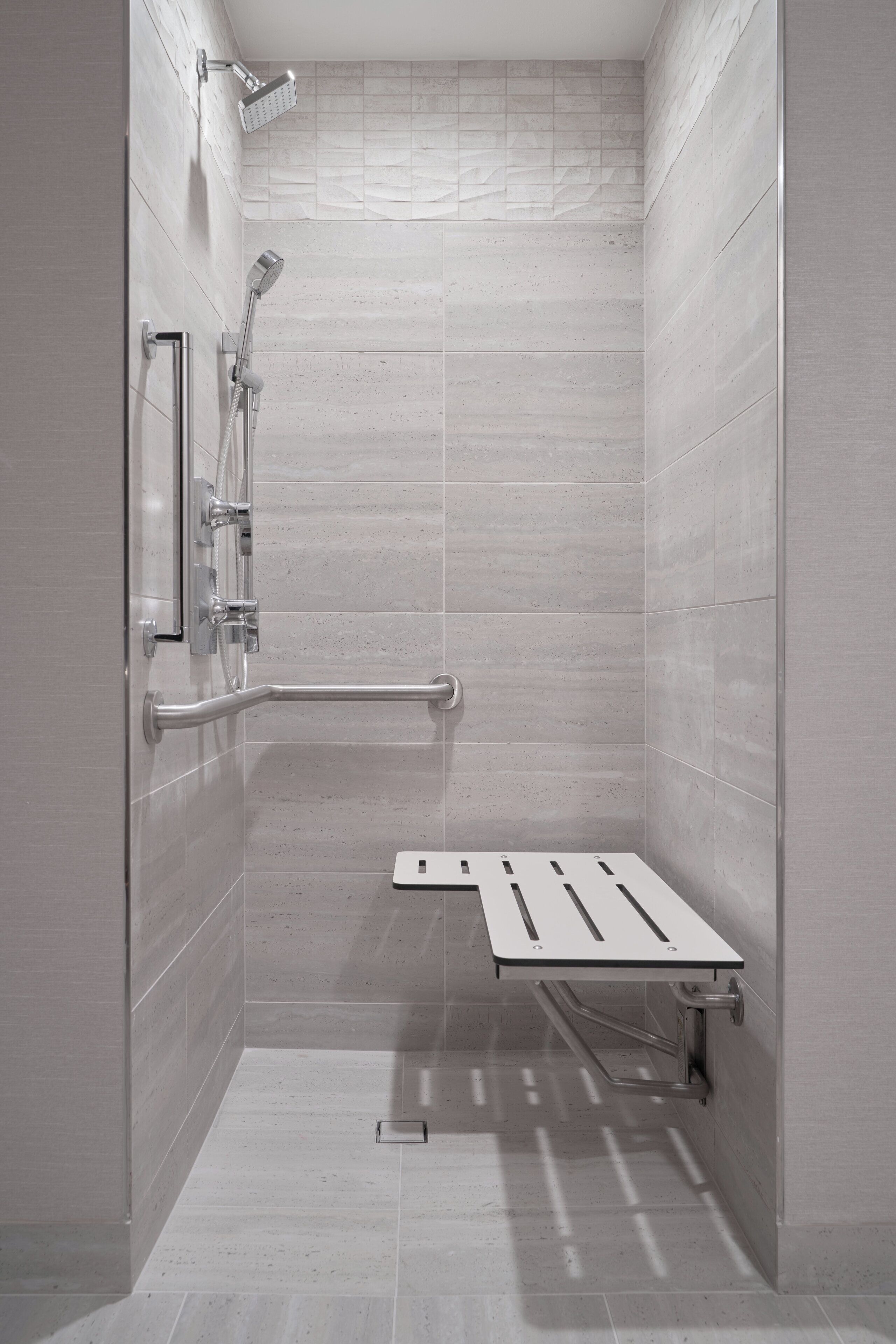 A modern shower with a handheld showerhead, a wall-mounted faucet, and a safety bar.