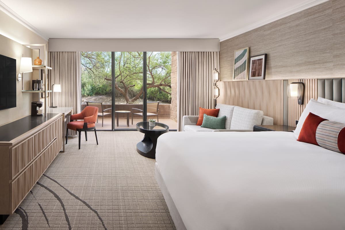 A hotel room with a large bed, a desk, a chair, a small table, and a view of the outdoors.