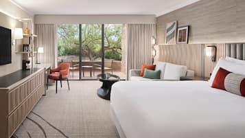 Habitación de hotel con una cama grande, un escritorio, una silla, una mesita y vistas al exterior.