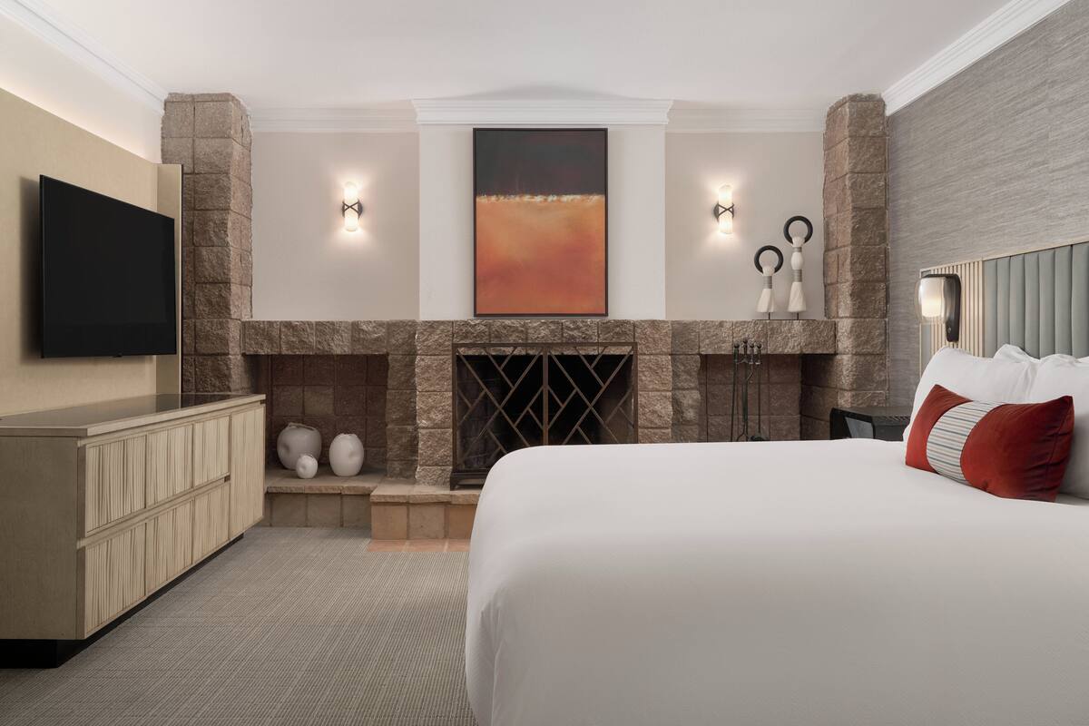 A hotel room with a large bed, a stone fireplace, a flat-screen TV, and a mounted artwork.