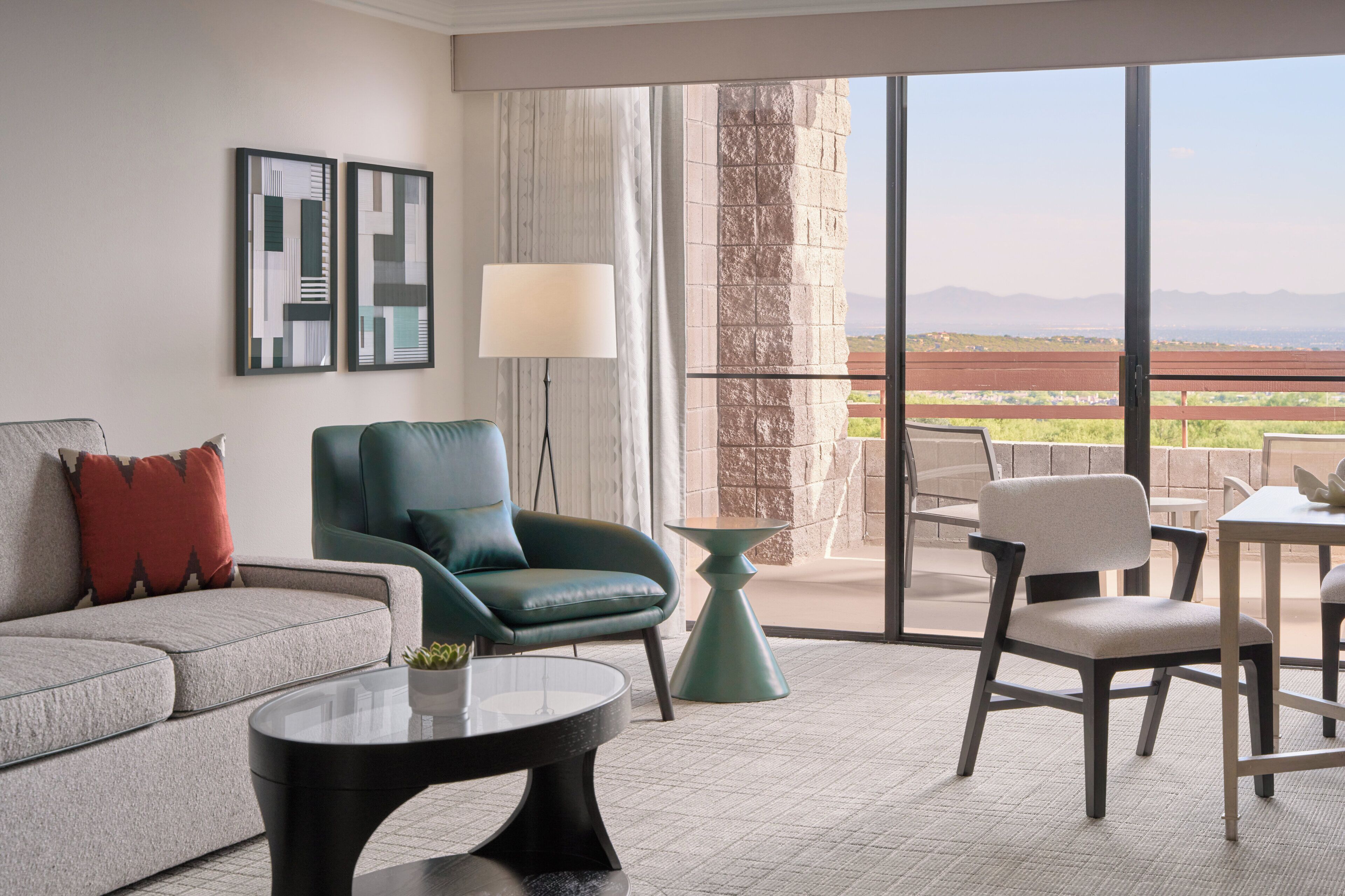 A modern living room with a sofa, armchair, coffee table, and a view of the outdoors through large windows.