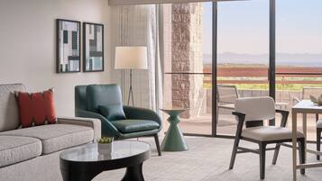 A modern living room with a sofa, armchair, coffee table, and a view of the outdoors through large windows.
