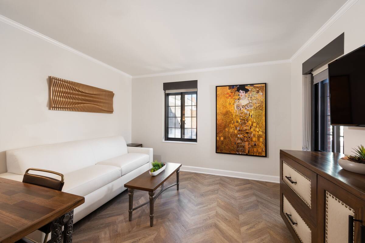 A modern living room with a white sofa, wooden coffee table, and a large painting on the wall.