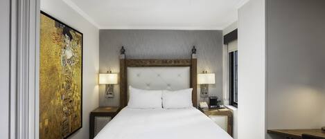Quarto de hotel com uma cama grande, duas mesas de cabeceira com abajures, um quadro grande na parede e uma escrivaninha com cadeira.