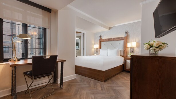 A hotel room with a large bed, a desk with a chair, a TV, and a window with blinds. - Westgate New York Grand Central (New York)