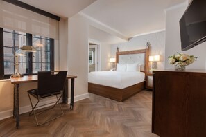 Een hotelkamer met een groot bed, een bureau met stoel, een televisie en een raam met jaloezieën.