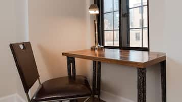 Una habitación de esquina con una mesa de madera, un sillón de cuero, una lámpara de pie y un ventanal con vistas a edificios.