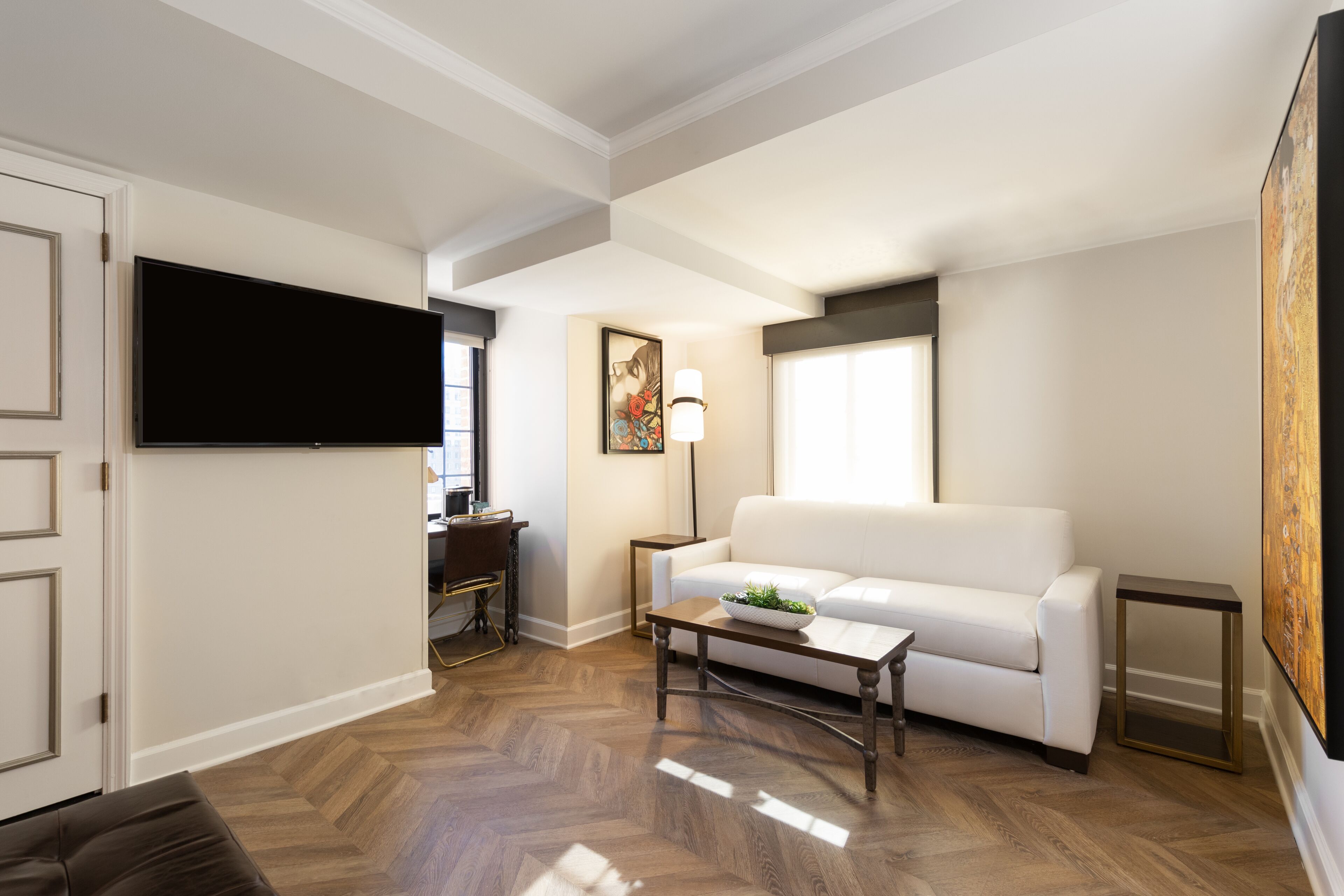 Un salon avec un téléviseur à écran plat, un canapé blanc, une table basse et un tableau accroché au mur.