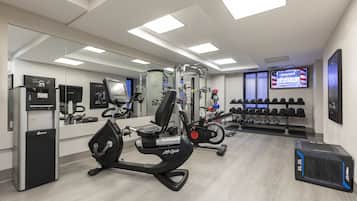 Un gimnasio con equipo cardiovascular, máquinas de pesas y un televisor en la pared.