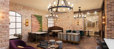 A modern lounge with brick walls, a large chandelier, and a mix of seating options including a purple armchair and a sofa.