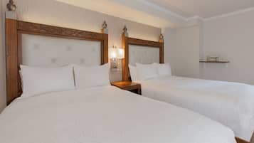 Habitación de hotel con dos camas tamaño queen, un cabecero de madera, una mesita de noche con lámpara y un estante sobre la cama.