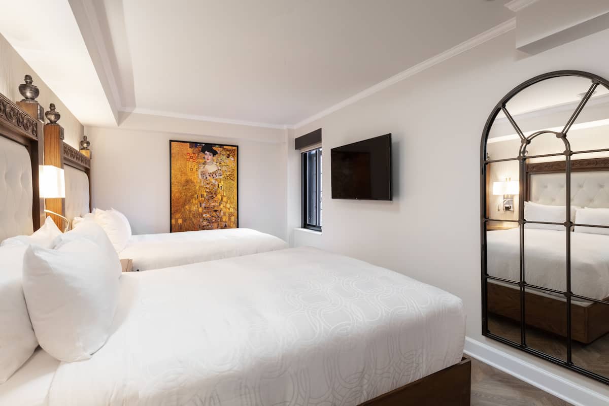 A hotel room with two beds, a painting on the wall, a TV mounted above the bed, and a large mirror on the wall.