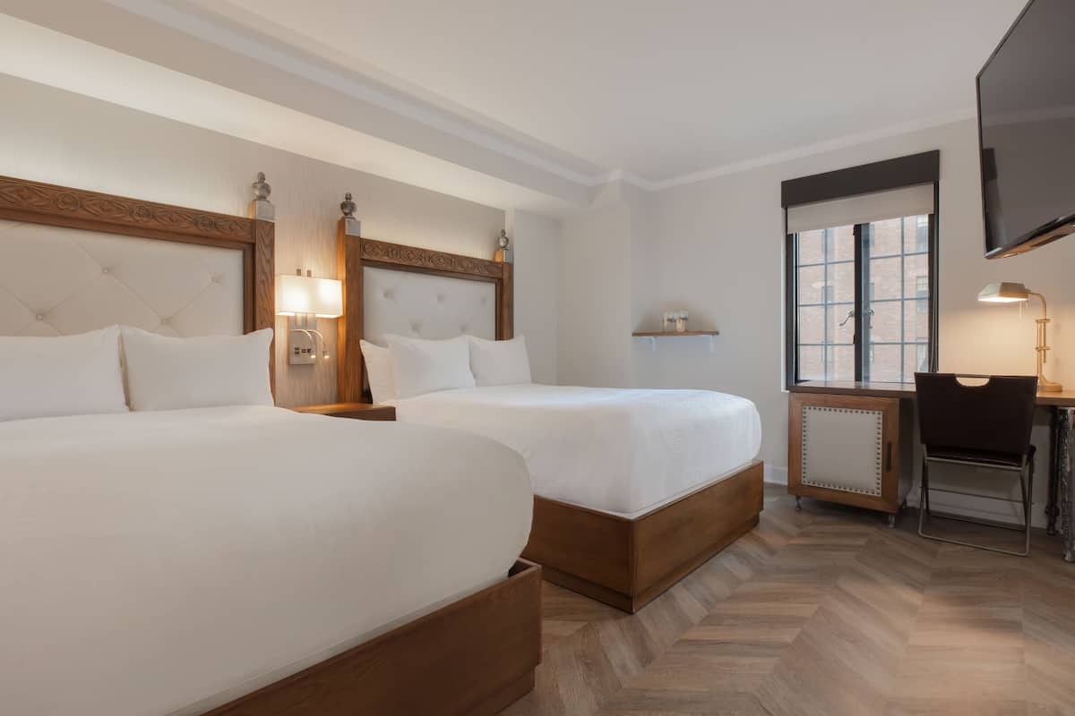 A hotel room with two beds, a desk, a chair, and a TV mounted on the wall.