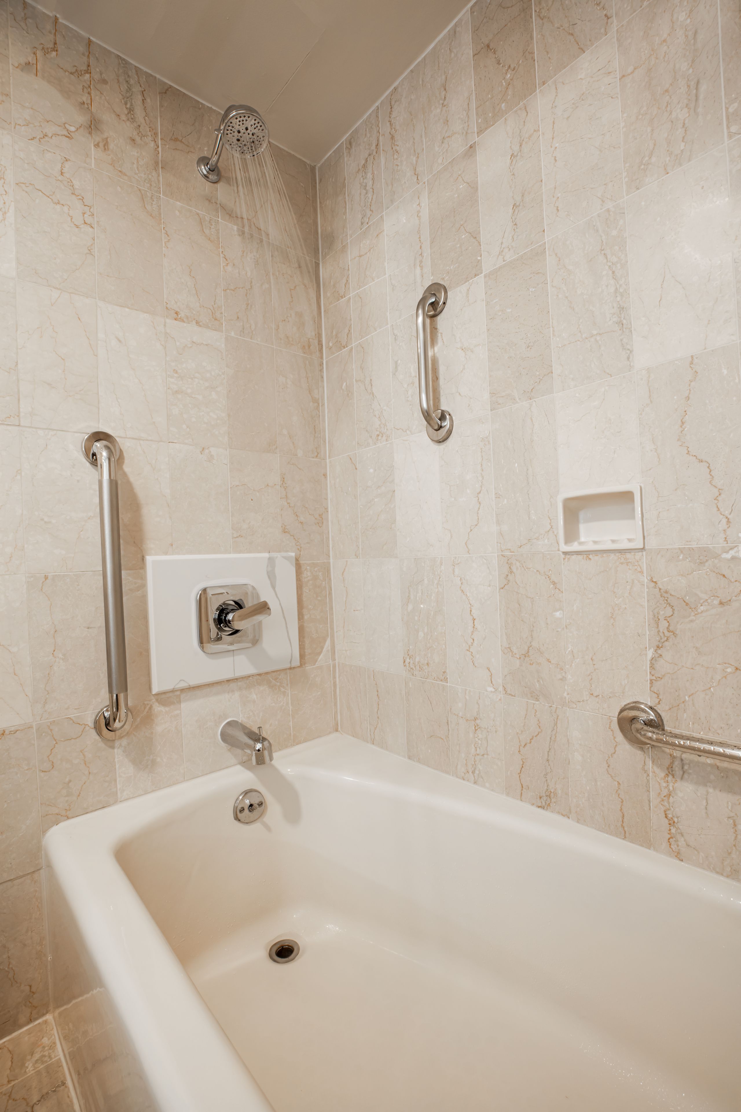 Un baño con bañera, barras de apoyo y cabezal de ducha.